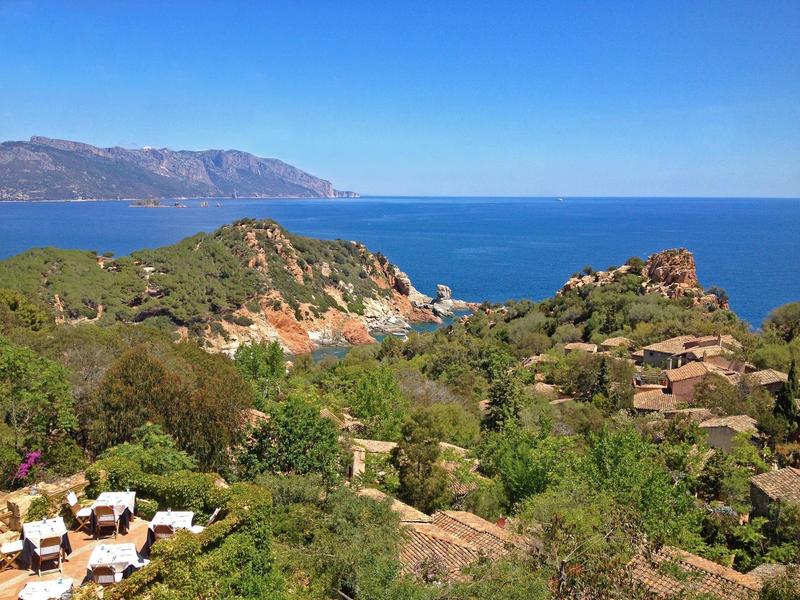 Küstenlandschaft mit Felsen, grünem Buschwerk und blauer See unter klarem Himmel.