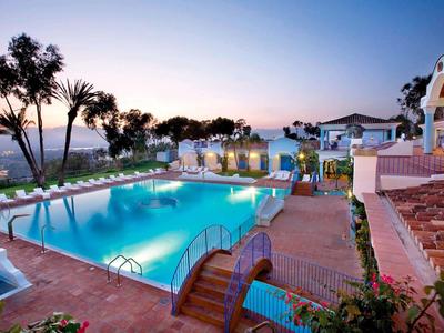 Área de piscina de lujo al atardecer con tumbonas y palmeras en un complejo hotelero.