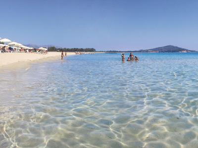 Clear shallow water at a sandy beach with few people and blue sky.