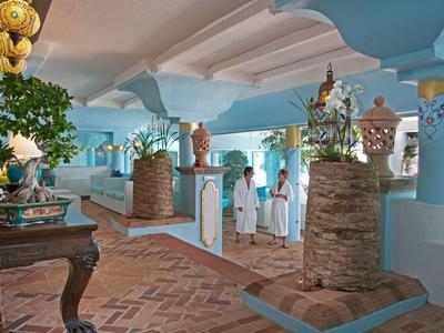 Área interior de hotel con columnas azules, muros de piedra y tres personas en recepción.
