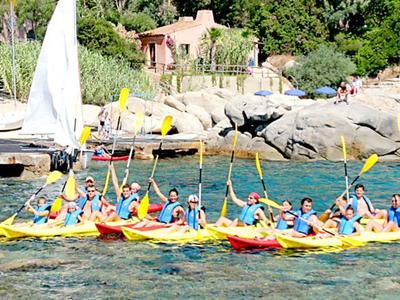 Group of people in yellow kayaks paddling on clear water near a dock and rocky shore.