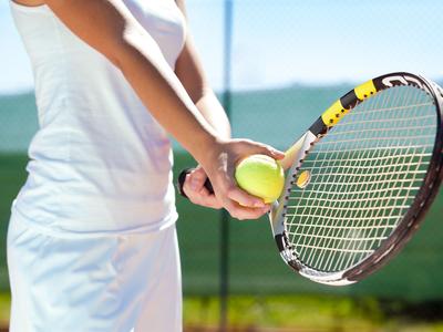 Person in white sportswear holding a tennis ball and racket ready to play.