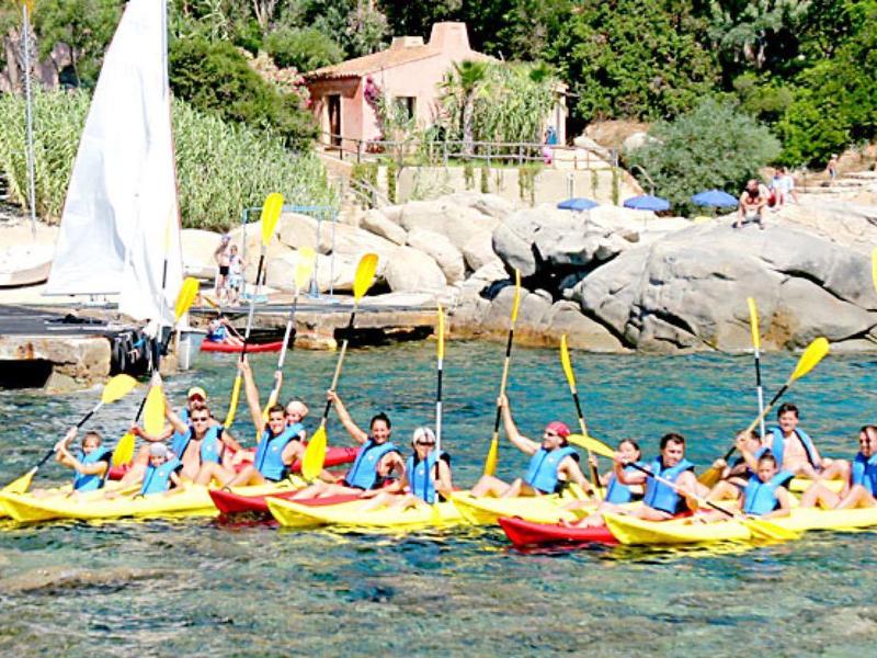 Grupo de personas en kayak sobre agua clara cerca de una costa rocosa y un pequeño muelle.