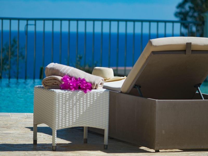 Ligstoel en bijzettafel met handdoeken en bloem bij een zwembad met uitzicht op zee.