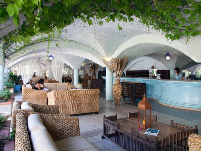 Open hotel lounge met rotan meubels en blauwe receptiebalie onder boogarchitectuur.