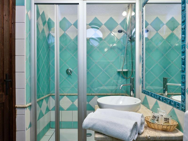 Kleine badkamer met douchecabine, groene tegels en wastafel op marmeren blad.