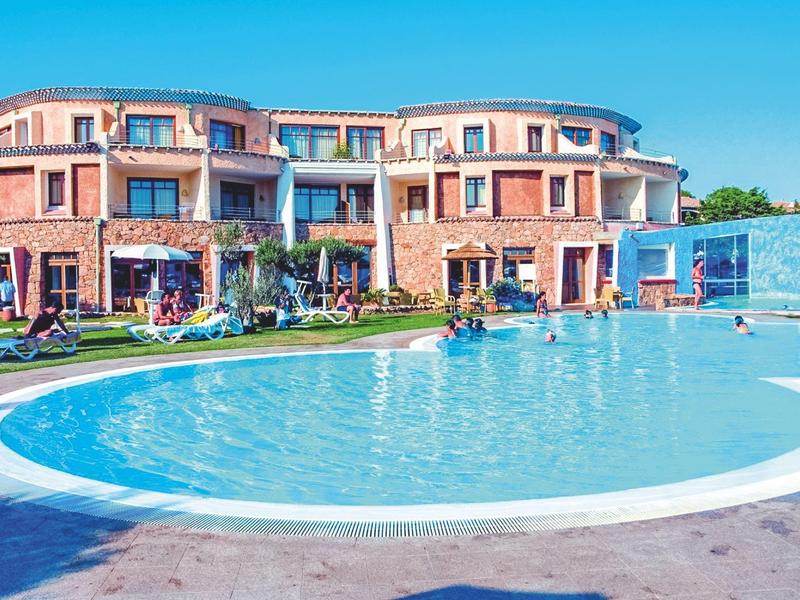 Hotel con piscina rotonda davanti a un edificio di più piani sotto un cielo azzurro.