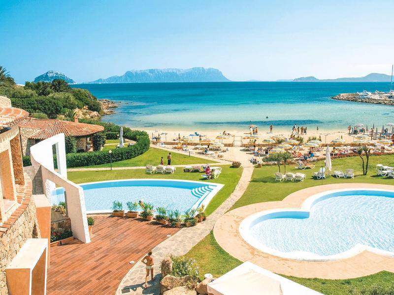Piscine e terrazza con vista su una spiaggia affollata e l'oceano all'orizzonte.