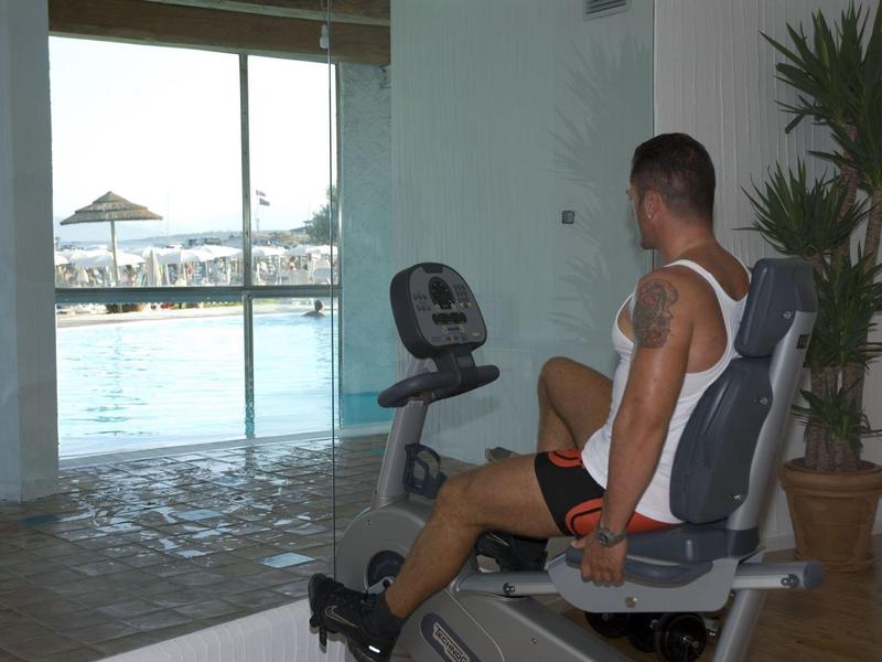 Uomo seduto su un attrezzo fitness vicino a grandi finestre con vista sulla spiaggia.