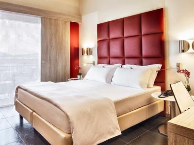 Camera d'albergo moderna con letto grande, testiera imbottita rossa e luce naturale dalla finestra