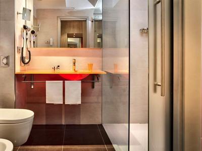 Bagno moderno con doccia in vetro, lavandino rosso e asciugamani bianchi.