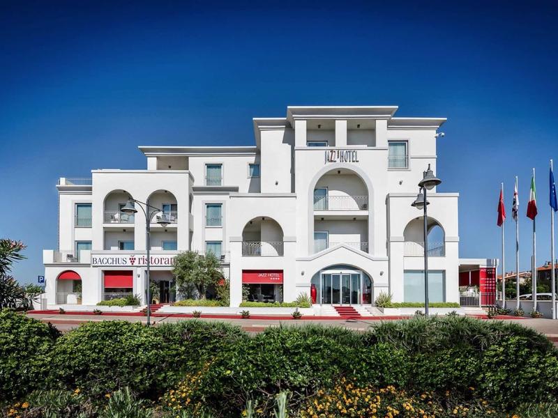 Hotel bianco moderno con archi multipli e tende rosse sotto un cielo blu sereno.