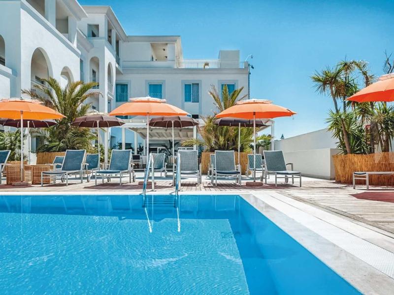 Piscina moderna dell'hotel con ombrelloni arancioni e lettini bianchi sotto un cielo limpido.