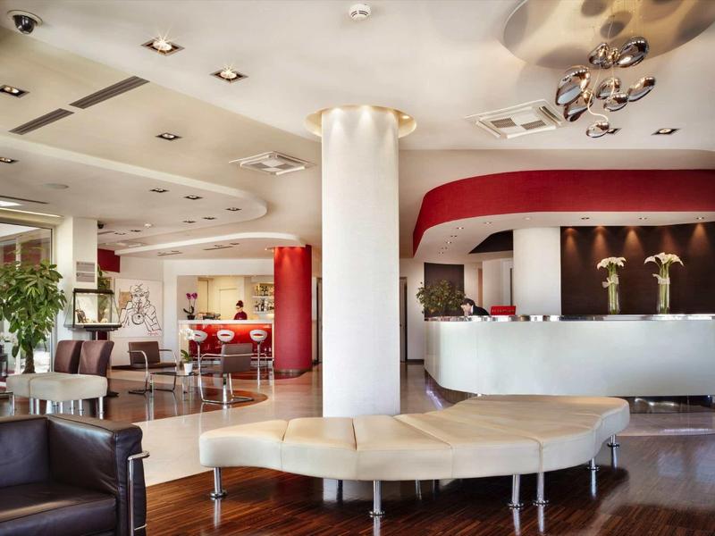 Moderna hall d'hotel con area salotto, banco reception e pavimento in legno caldo.