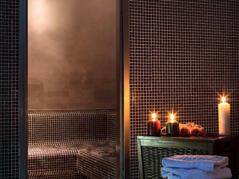 Sauna a vapore con porta in vetro chiusa, luce di candele e una pila di asciugamani bianchi.