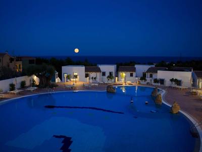 Piscine ronde d'hôtel la nuit avec bungalows illuminés et pleine lune en arrière-plan.