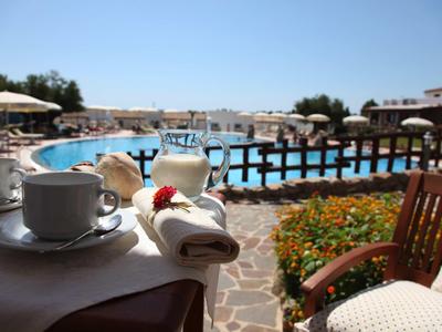 Tazza di caffè e tovagliolo accanto a una piscina con sedie e ombrelloni su una terrazza.