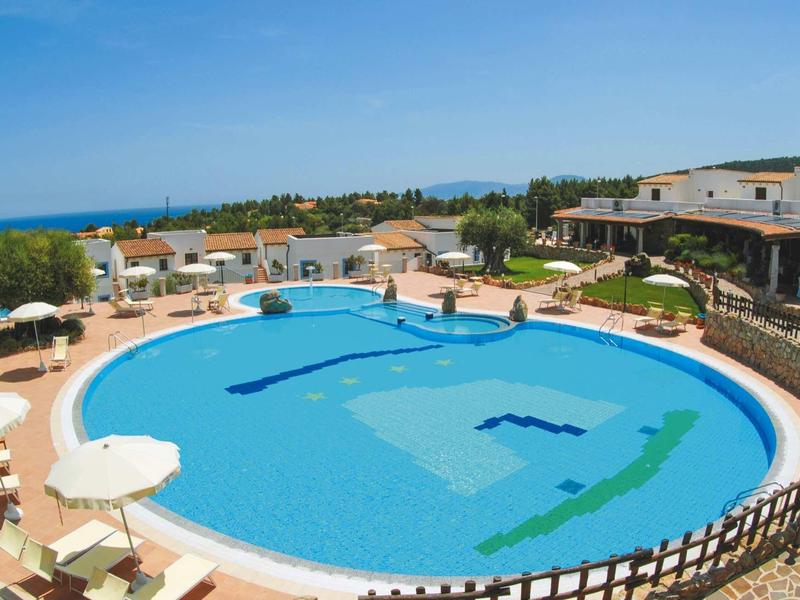 Grande piscine ronde avec parasols et chaises longues dans un jardin d'hôtel au bord de la mer.