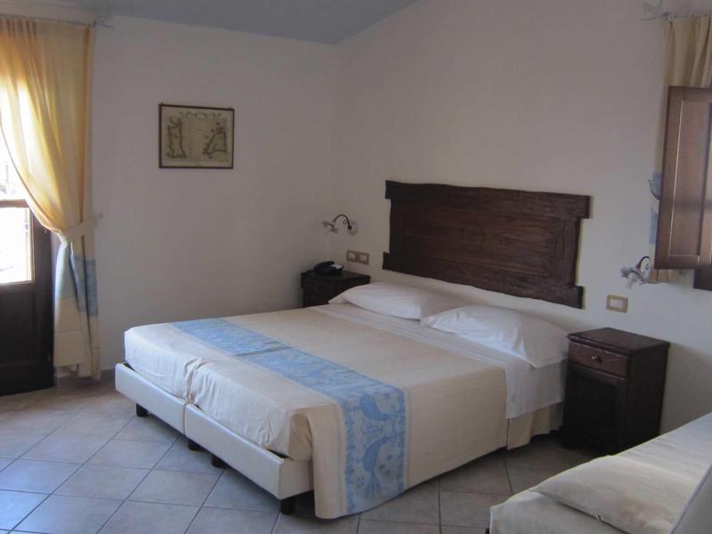 Chambre d'hôtel lumineuse avec lit double, tables de chevet, rideaux et panneau en bois décoratif au mur.