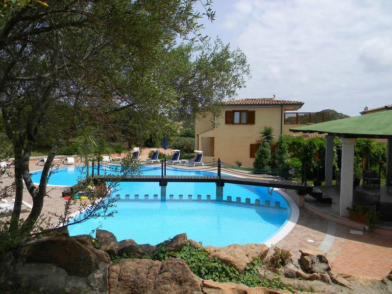Hotel pool with bridge, sun loungers, surrounded by trees and buildings