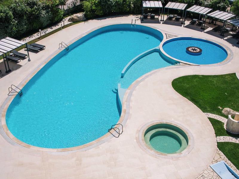 Duży basen z sąsiednim brodzikiem i okrągłą wanną z hydromasażem obok leżaków na zewnątrz.