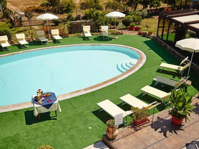 Espace piscine avec transats, parasols et table avec en-cas, entouré de verdure.