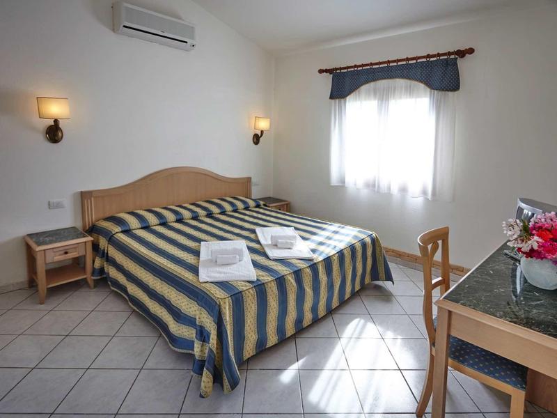 Chambre lumineuse avec lit double, deux tables de chevet et un bureau décoré de fleurs.