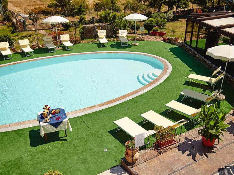 Vue sur une piscine ronde avec des chaises longues et des parasols dans un jardin.