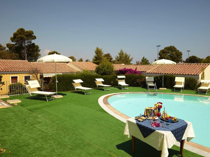 Piscine ronde dans le jardin de l'hôtel avec chaises longues et table dressée sous un ciel bleu clair.