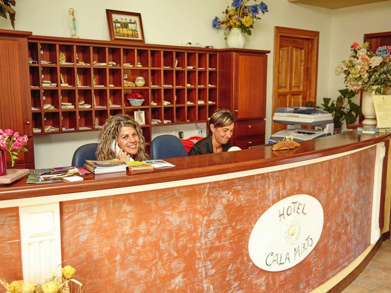 Réception d'hôtel avec deux employés derrière un comptoir incurvé et des arrangements floraux.