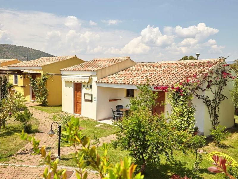 Petite maison de vacances avec jardin et végétation méditerranéenne sous un ciel bleu.