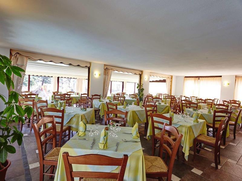 Grande salle à manger avec plusieurs tables et chaises, éclairée par de grandes fenêtres.