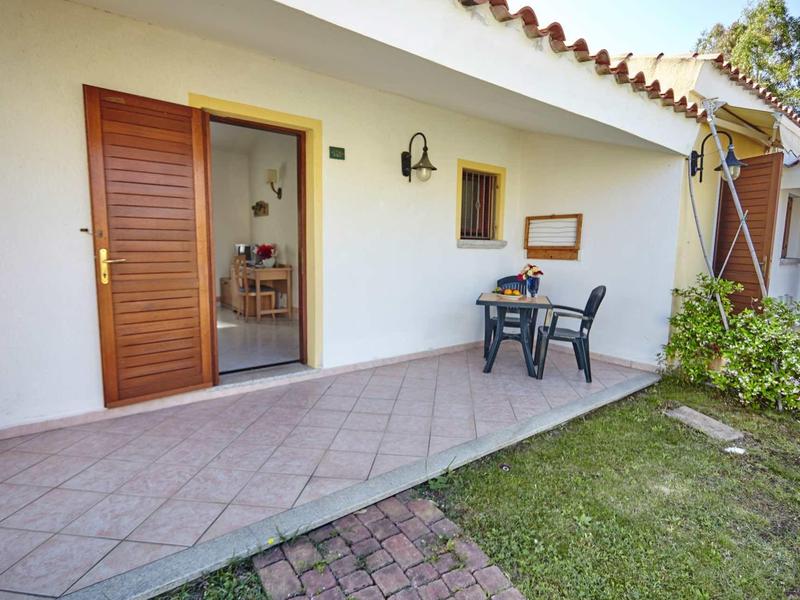 Terrasse avec table et chaises devant une maison avec une porte en bois ouverte.