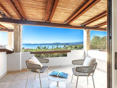Balkon mit Blick auf Garten und Meer, ausgestattet mit modernen Stühlen und Tisch.