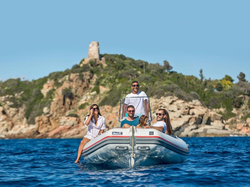 Quatre personnes sur un bateau pneumatique par temps clair près d'une côte rocheuse sous un ciel bleu.
