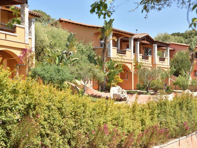 Rangées de maisons de vacances jaunes et orange avec des arches et terrasses entourées de verdure.