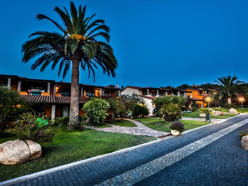 Complexe hôtelière éclairée avec jardin, palmiers et sentier pavé au crépuscule