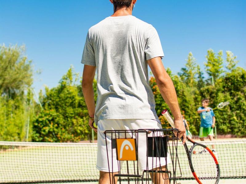 Personne sur un court de tennis tenant une raquette près d'un panier de balles.