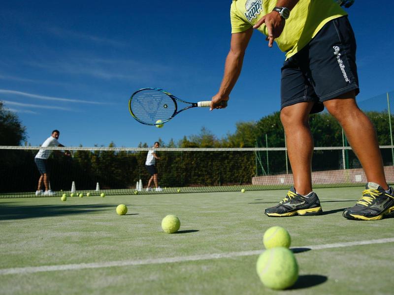 Personne jouant au tennis sur un court extérieur par une journée ensoleillée.