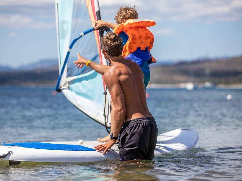 Un homme apprend la planche à voile à un enfant sur une eau calme.