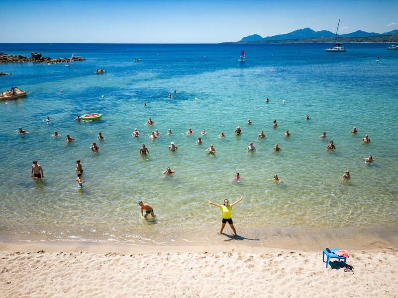 De nombreuses personnes nagent et se détendent dans une eau claire à la plage par temps ensoleillé.