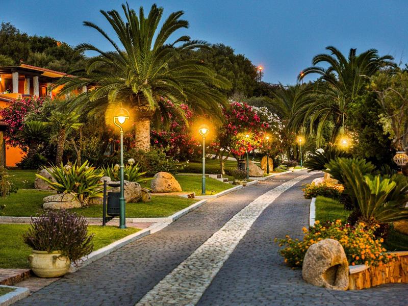 Allée de jardin éclairée avec des palmiers et des plantes à côté des hôtels le soir.