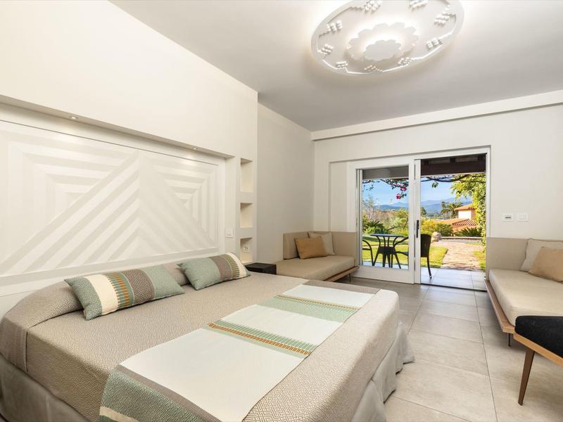 Chambre d'hôtel moderne avec lit double, coin salon et vue sur la terrasse et le jardin.