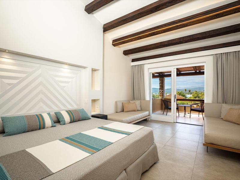 Chambre d'hôtel lumineuse avec lit double, coin salon et balcon avec vue sur la mer.