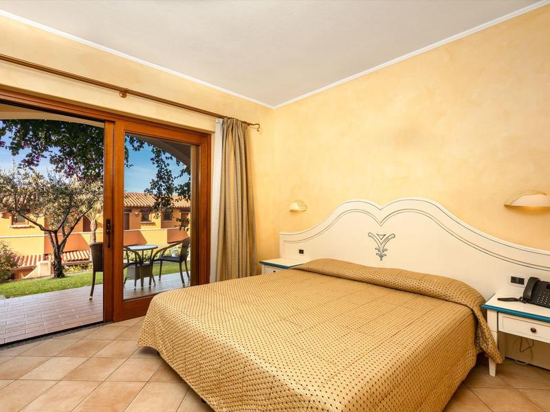 Chambre d'hôtel lumineuse avec grand lit et vue sur terrasse et jardin.