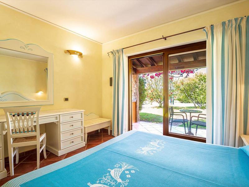 Chambre d'hôtel lumineuse avec bureau, chaise et vue sur terrasse et jardin.