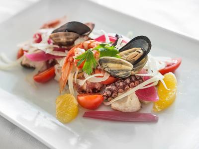 Elegantní miska mořských plodů s mušlemi, chobotnicí, rajčaty a citrusy na bílém talíři.