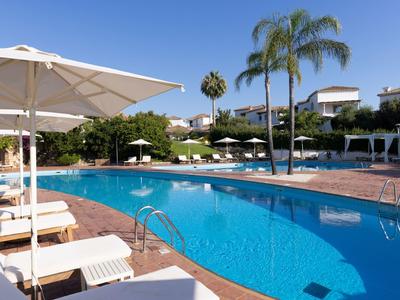 Moderní hotelový bazén s lehátky, slunečníky a palmami pod modrou oblohou.