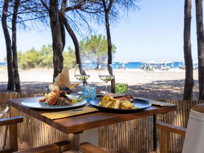 Ein gedeckter Tisch mit Getränken und Essen an einem schattigen Strandplatz mit Blick aufs Meer.