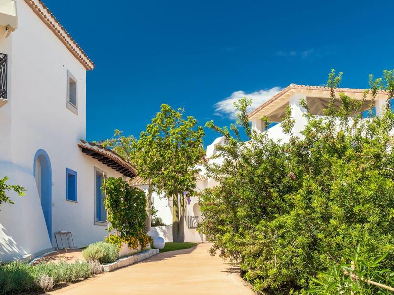 Bílé domy s modrými okny a zelenou vegetací pod jasně modrou oblohou.